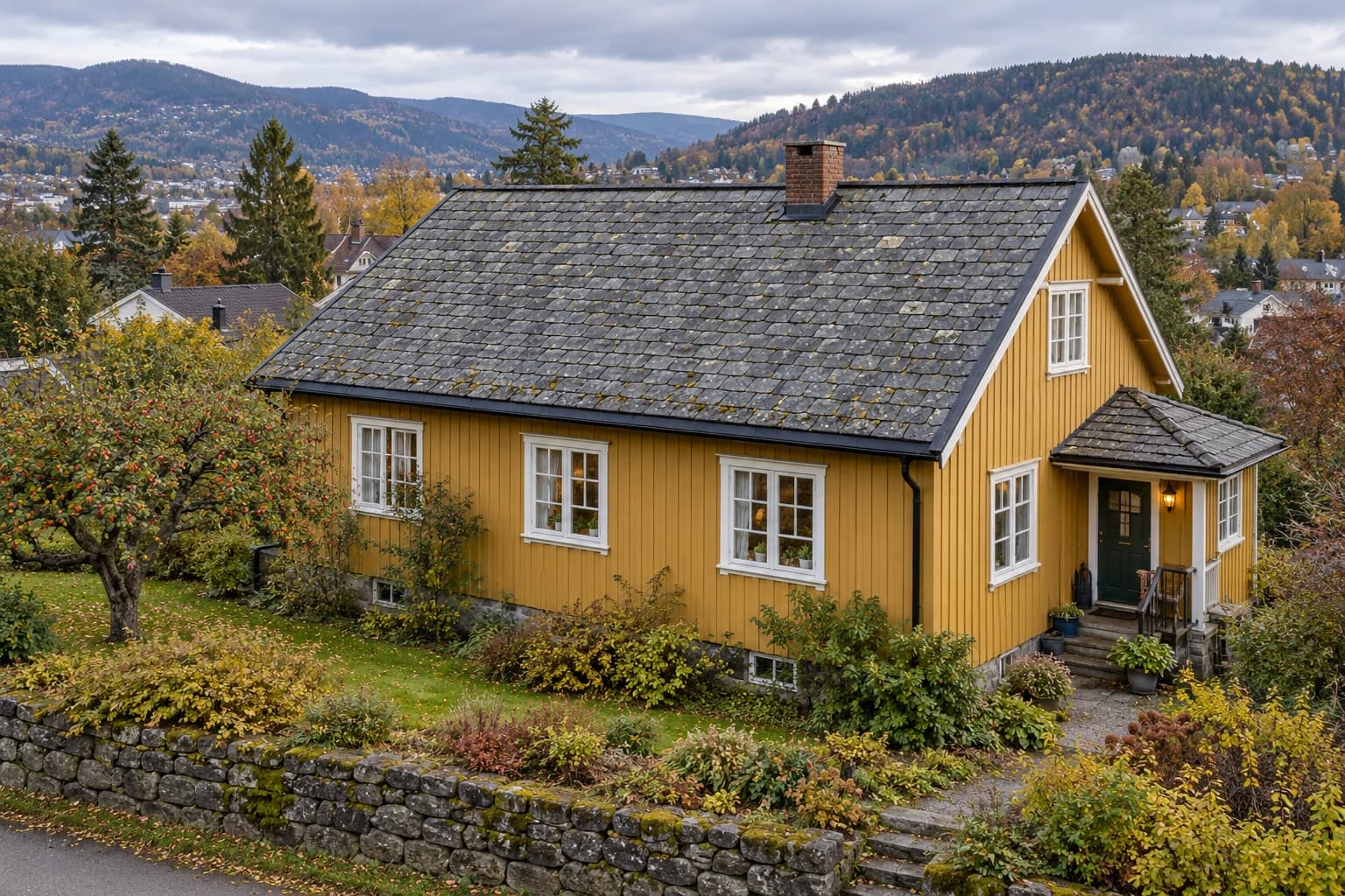 Eldre okerfarget trehus med værslitt skifertak, murpipe og en liten veranda i en høsthage.